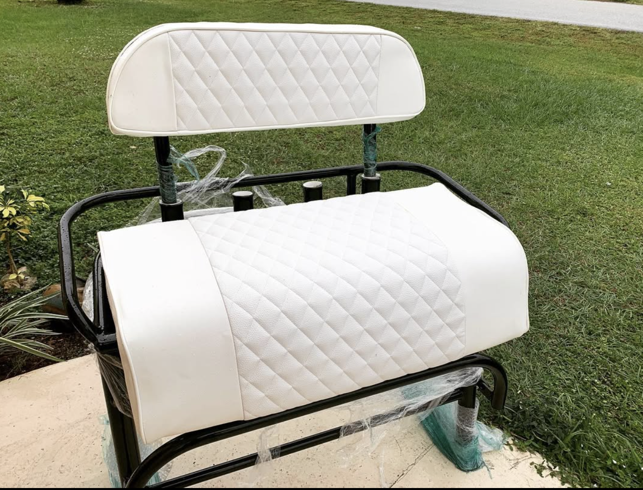 White quilted golf cart seat and backrest with black metal frame on grass
