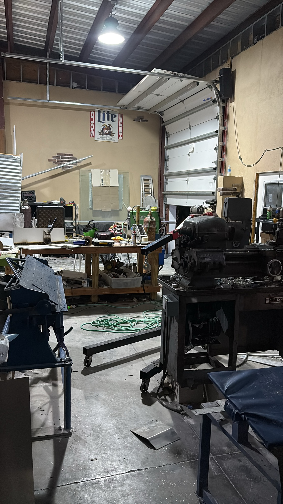 Industrial workshop garage with workbenches, tools, and equipment under metal roof