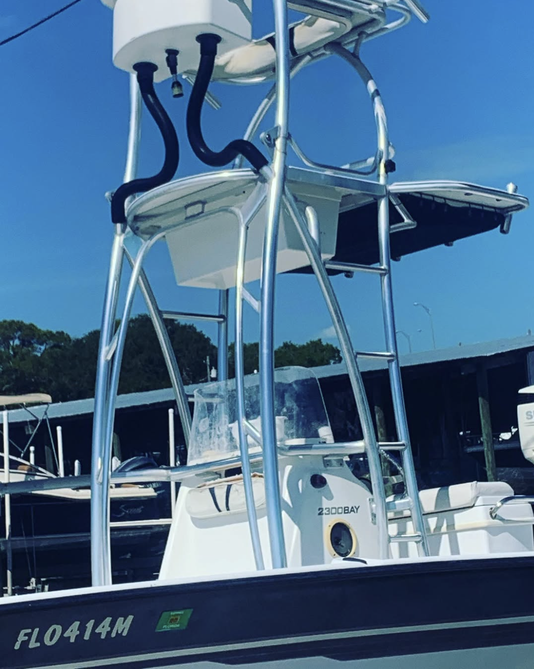 Sportfish boat with tall tower, twin black handles, hardtop canopy, and registration number 2300BAY docked at marina