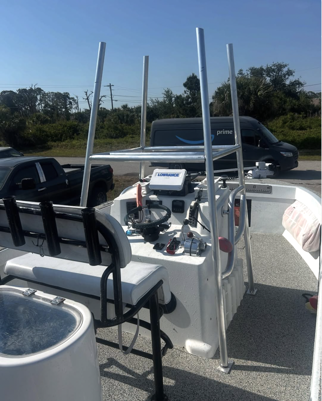 White fishing boat with Lowrance GPS display, aluminum T-top frame, and black seat cushions at dock