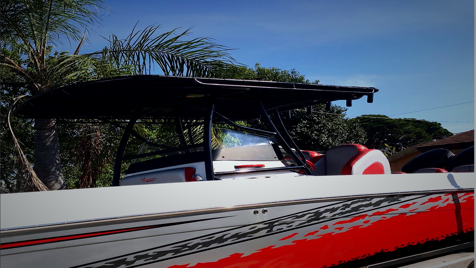 Red and white speedboat with black convertible top parked under palm trees