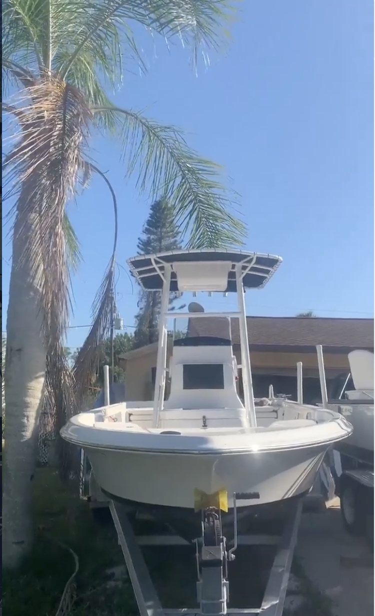 White center console fishing boat on trailer under palm tree in driveway